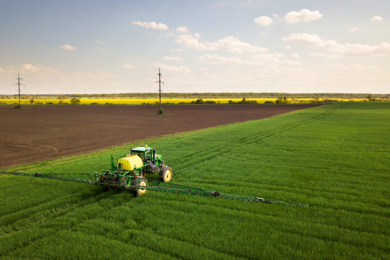 Tractor spraying chemical pesticides with sprayer on the large green agricultural field at spring