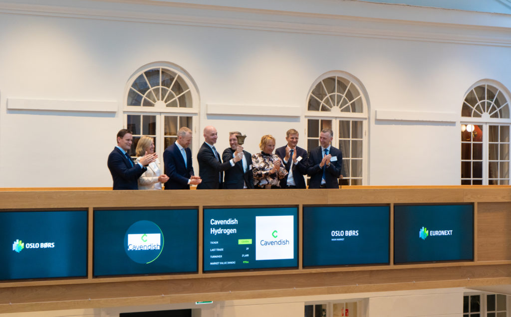 Eight people standing on a balcony, smiling and clapping. Launch of Cavendish Hydrogen on Oslo Børs.