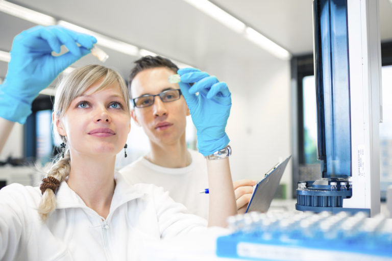 Two young chemistry researchers, a young woman and and a young man carrying out experiments in a lab