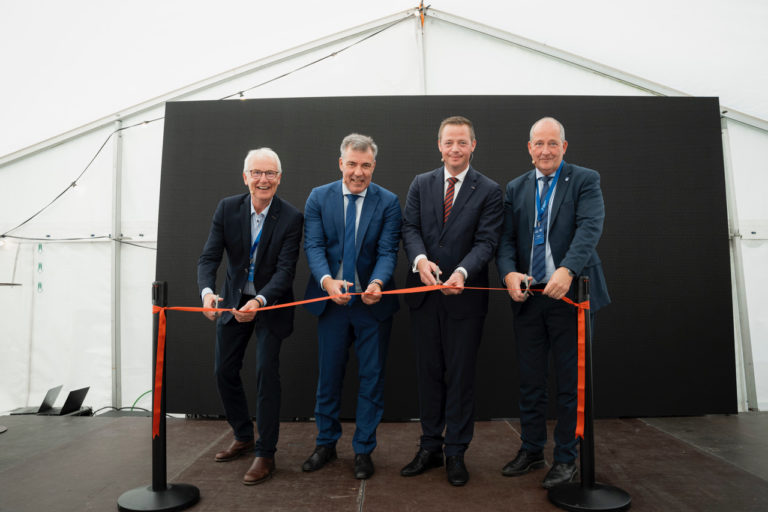 Four smiling business men in suits cutting a red ribbon